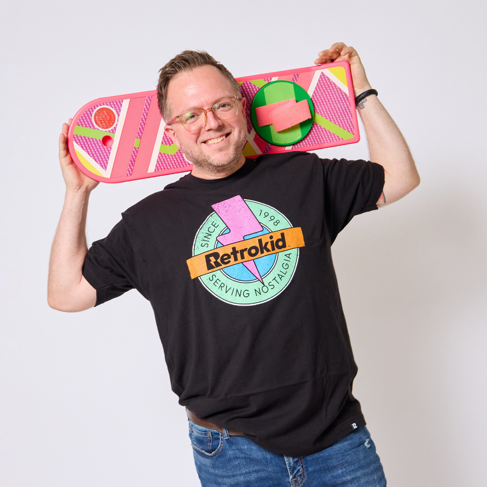 Man wearing a black 90s Retrokid Originals t-shirt with 'Retrokid' logo holding pink and green toy hover board against a white background