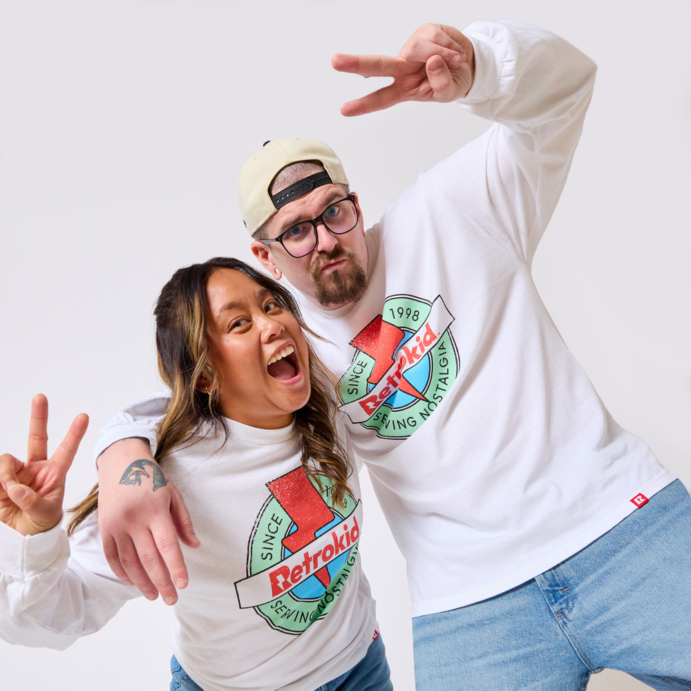 Two people wearing white Retrokid Originals '90s long sleeve shirts with a colorful logo on a plain background